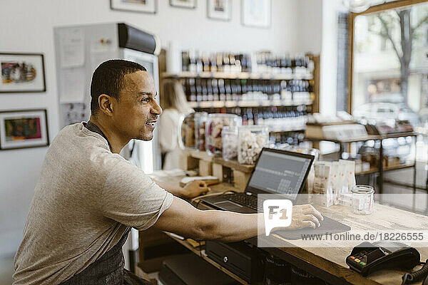 Side view of male owner sitting at checkout counter in deli