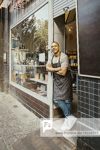 Smiling male owner with arms crossed leaning at shop doorway