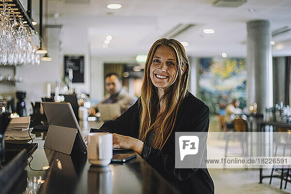 Porträt einer lächelnden weiblichen Fachkraft  die mit einem Laptop an der Theke eines Restaurants sitzt