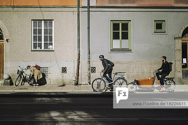 Männliche Pendler auf Fahrrädern auf der Straße vor einem Gebäude an einem sonnigen Tag