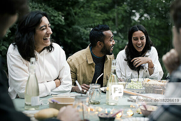 Junger Mann genießt mit weiblichen Freunden während einer Dinnerparty im Hinterhof
