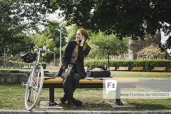 Glückliche Geschäftsfrau  die mit dem Handy telefoniert  während sie mit dem Fahrrad im Park sitzt