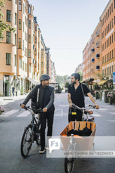 Male business colleagues with bicycles talking while standing on road
