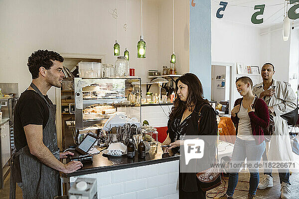 Männlicher Cafébesitzer im Gespräch mit einer in der Warteschlange stehenden Kundin