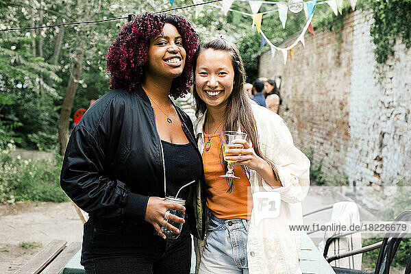Porträt von glücklichen multirassischen Freundinnen mit Getränken  die während einer Party im Hinterhof zusammenstehen