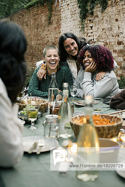 Glückliche weibliche Freunde genießen zusammen am Esstisch während Abendessen Partei im Hinterhof