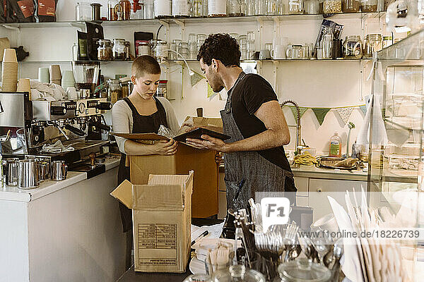 Seitenansicht eines männlichen Besitzers  der einer weiblichen Kollegin in einem Café mit einer Pappschachtel hilft