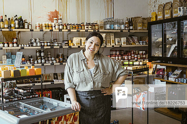 Porträt einer Besitzerin mit Hand auf der Hüfte  die neben einem Eiscreme-Gefrierschrank in einem Geschäft steht