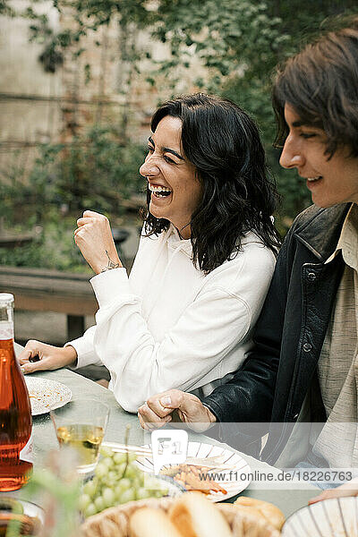 Glückliche Frau lacht  während sie mit einem männlichen Freund bei einer Dinnerparty am Esstisch sitzt