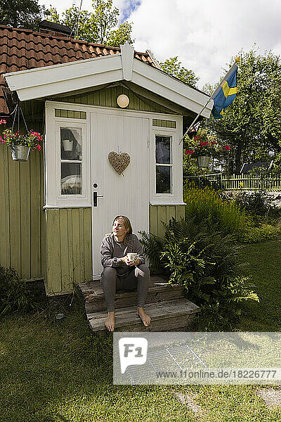 Frau mit geschlossenen Augen sitzt auf den Stufen vor dem Haus