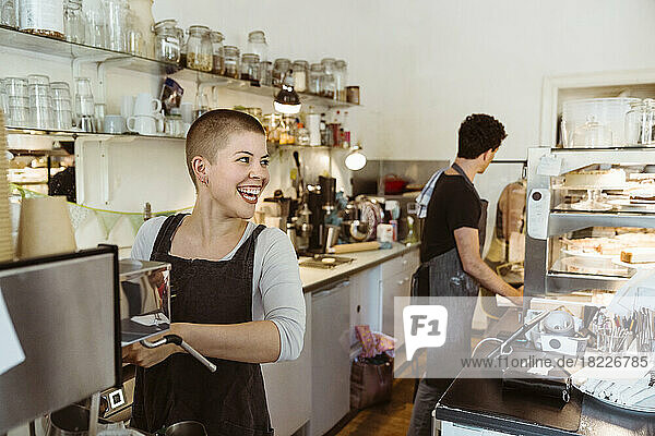 Junge glückliche Besitzerin schaut weg  während sie in einem Café Kaffee zubereitet