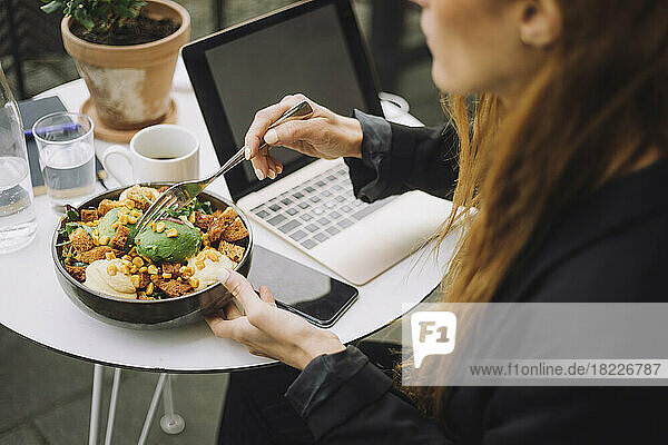 Geschäftsfrau mit Schüssel mit Essen und Laptop am Tisch