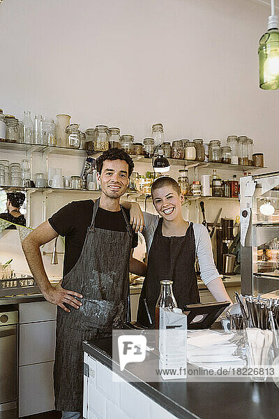 Portrait of happy male and female business owners standing together at cafe