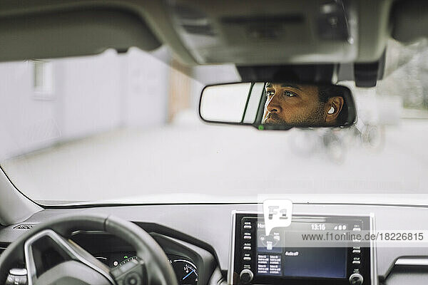 Reflexion eines männlichen Pendlers im Rückspiegel eines Autos