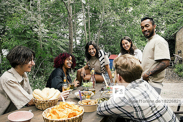 Glückliche männliche und weibliche Freunde  die sich beim Essen während einer Gartenparty im Hinterhof vergnügen
