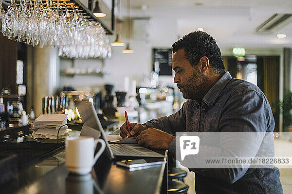 Businessman writing while sitting with laptop at bar counter
