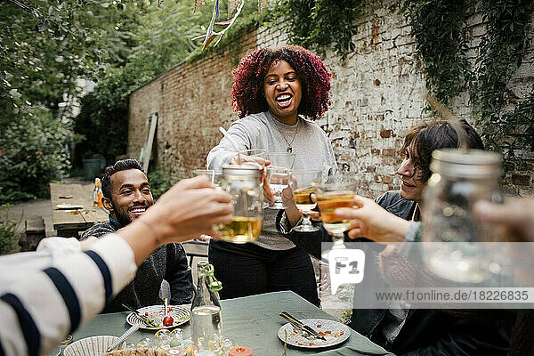 Frau mit lockigem Haar stößt mit Freunden bei einem geselligen Beisammensein im Hinterhof auf Getränke an