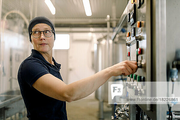 Female farmer wearing eyeglasses operating machine at dairy factory