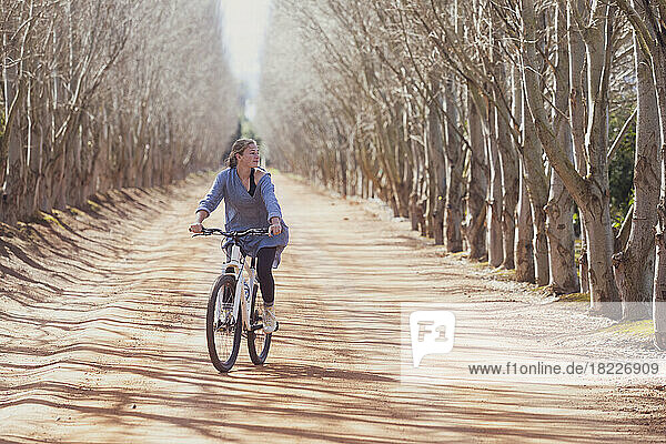Teenage girl (16-17) riding bicycle on tree lined road