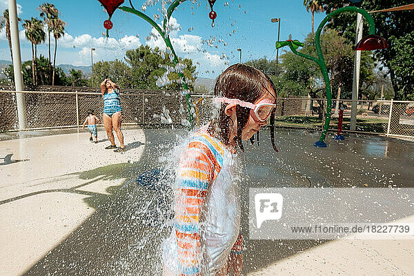 Goofy young girl being sprayed with water on a sunny day