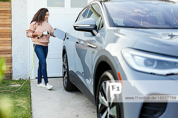 Woman holding charging cable by electric car in front yard
