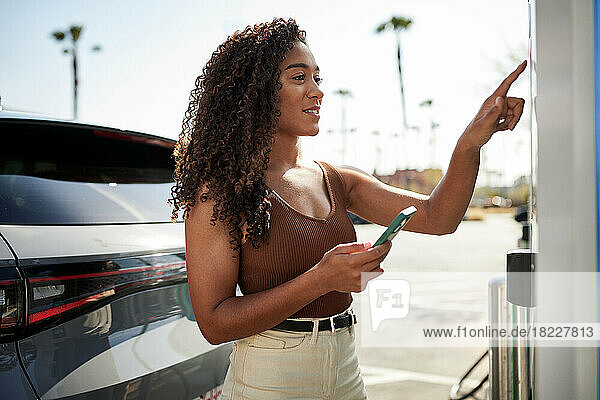 Woman with smart phone operating touch screen at charging station