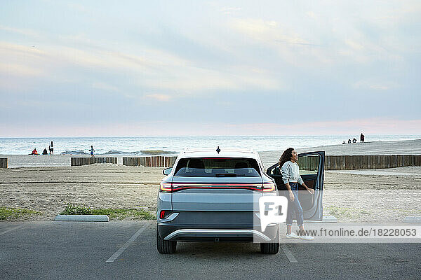 Young woman opening car door at parking lot by beach
