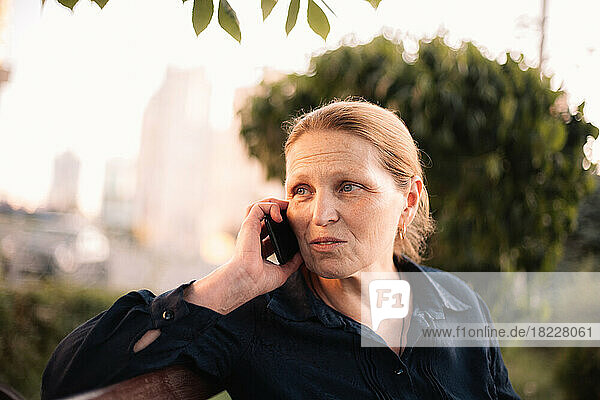 Mature business woman talking on smart phone sitting on bench in city