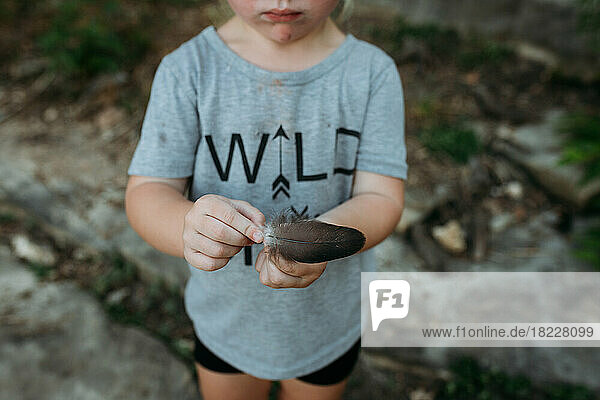 Little girl holding a bird feather on a hike