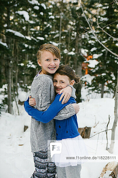 Kids hug in snow covered forest in sweaters and warm clothes