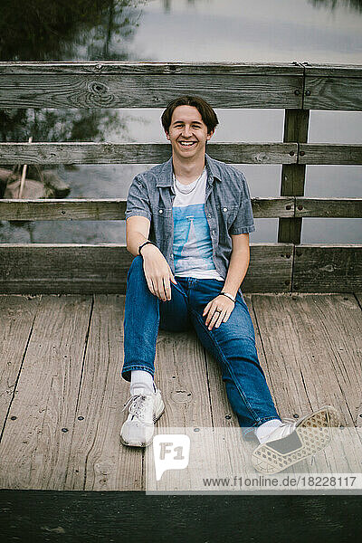 Teenage boy sits and smiles on a wooden dock on lake