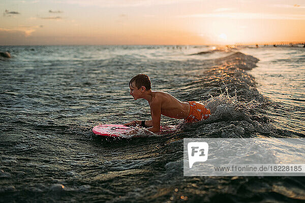 Young boy wake boarding in ocean waves at sunset