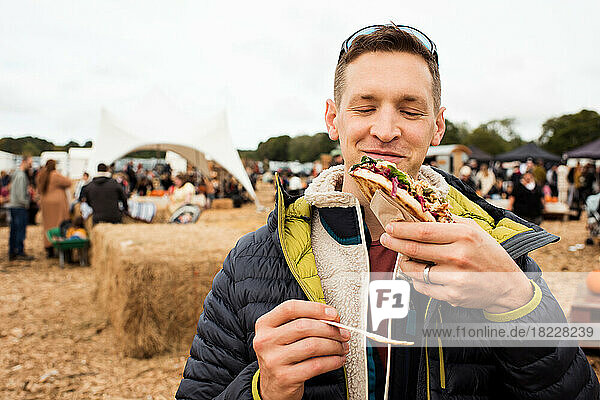 man holding street food whilst smiling at a festival