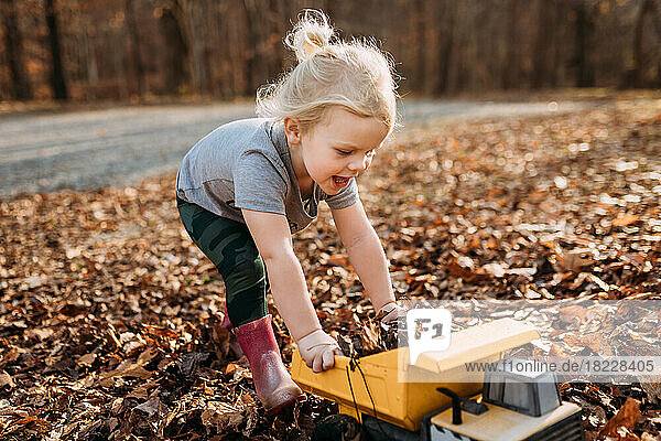 Happy child playing in fall leaves with toy truck