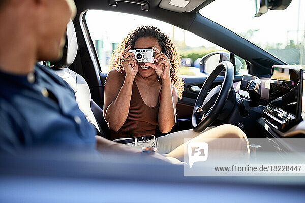 Smiling woman photographing boyfriend through camera during road trip