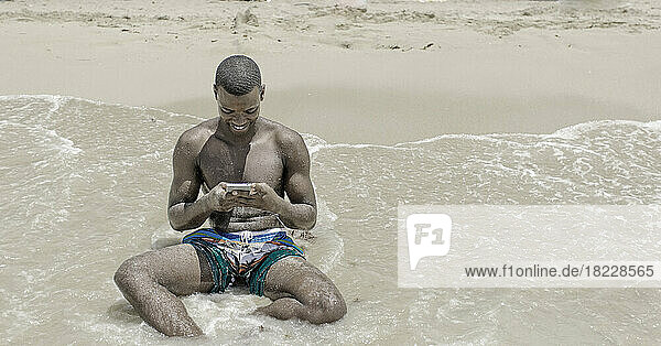 African-american man using a smartphone near the sea waves