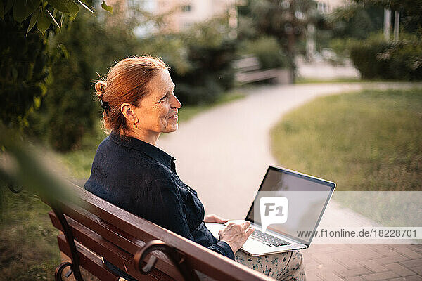 Happy mature business woman using laptop computer sitting on bench