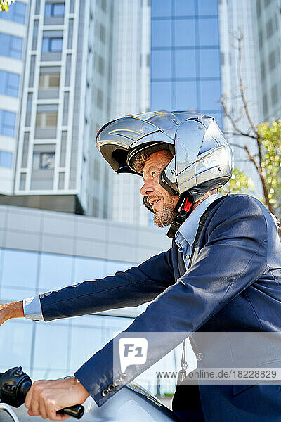 Modern businessman in full suit while sitting on motorbike outdoors