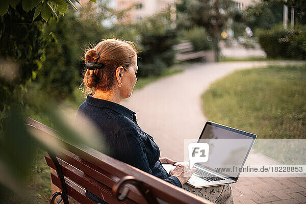 Mature business woman using laptop computer sitting on bench in park