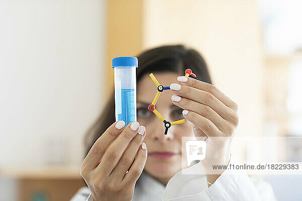 Chemist holding test tube and molecular model  focus on foreground