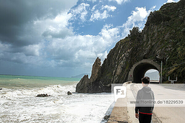 Rear view of boy (12-13) standing on coastal road  Sicily  Italy