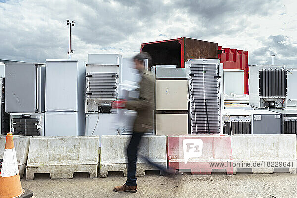 UK  Grimsby  Man passing by stacks of old refrigerators at recycling center
