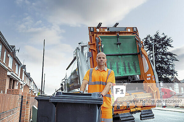 Portrait of refuse collector with bin and refuse truck