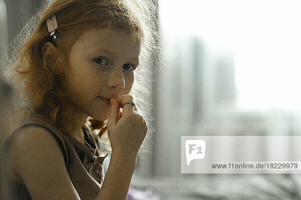 Smiling cute girl sitting on bed in front of window at home
