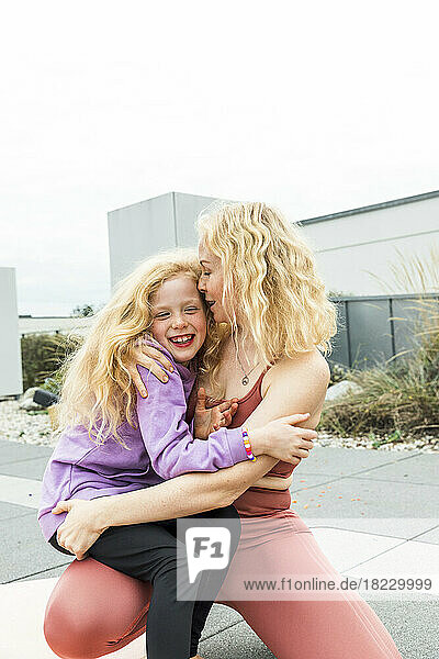 Mother whispering in daughter's ear crouching on rooftop