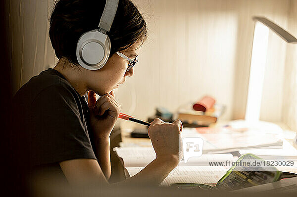 Boy wearing wireless headphones doing homework at home