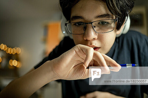 Boy wearing eyeglasses holding pen at home