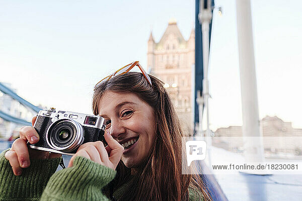Happy young woman holding camera on Tower Bridge  London  England