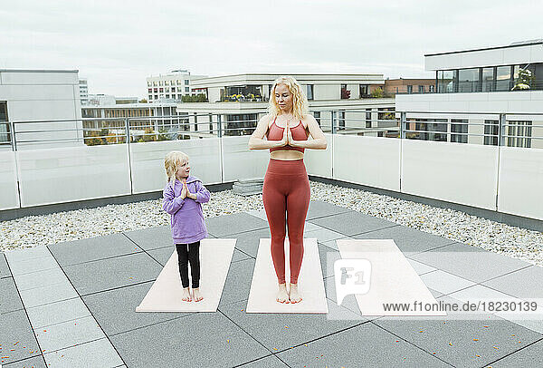 Cute girl practicing yoga with mother on rooftop