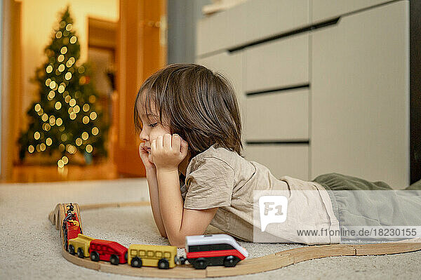 Nachdenklicher Junge schaut auf die hölzerne Spielzeugeisenbahn  die auf dem Boden liegt